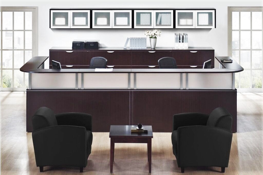 Double reception desk in espresso laminate with silver post transaction counters, rear lateral file storage bank, and wall hung overhead cabinets with aluminum framed doors.